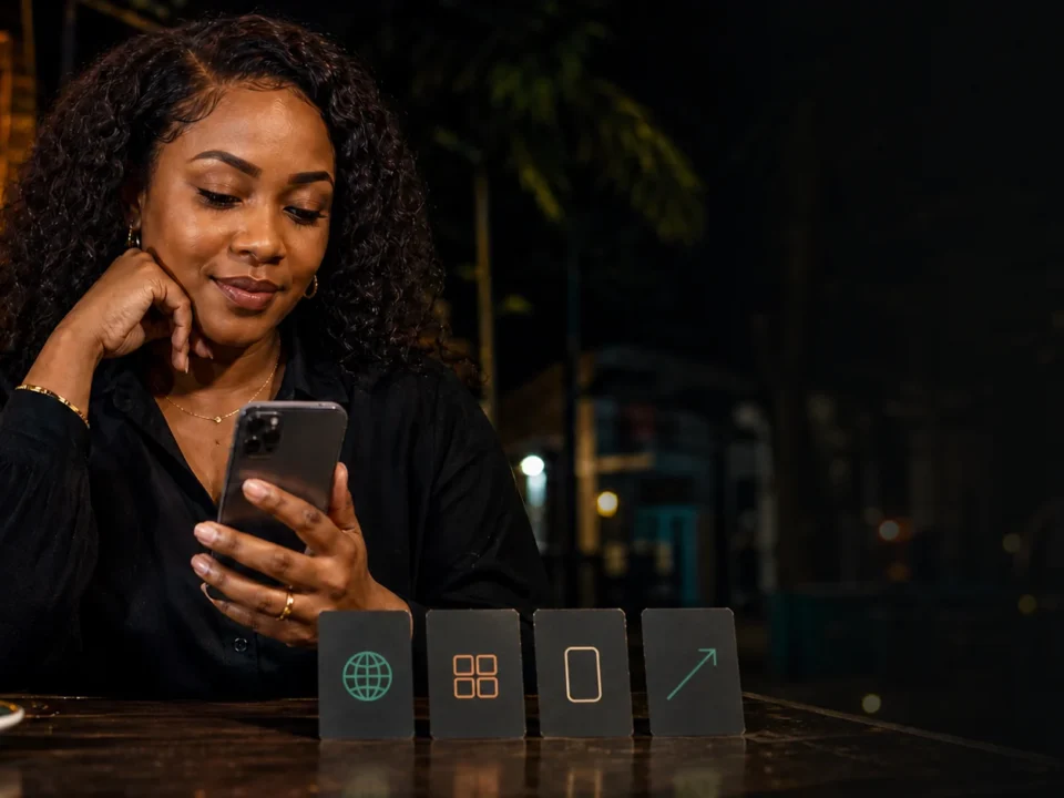 Mwanamke mzima akitumia simu mezani usiku mbele ya kadi nne za kubuni zinazoashiria njia za kufikia app