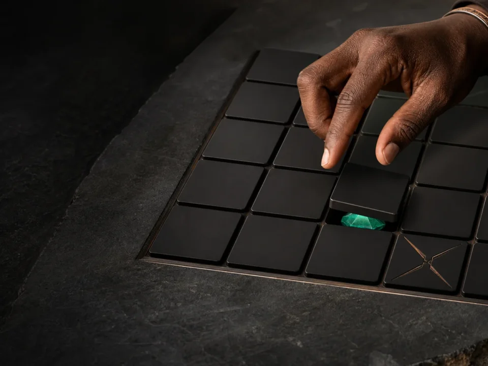 Mchoro wa kubuni wa mkono wa mtu mzima juu ya grid ya tiles nyeusi, gem moja ya kijani na tile moja ya hatari